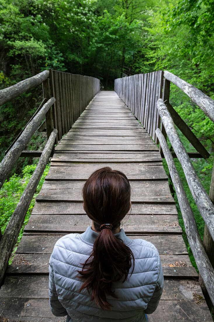 A girl crossing a wooden bridge on the trail of the Breggia gorges, Muggio Valley, Mendrisio District, Canton Ticino, Switzerland.