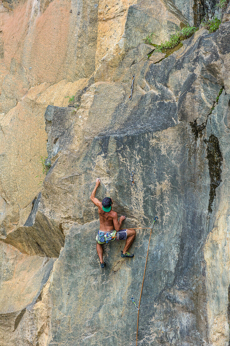 Rear view of shirtless adventurous man climbing rock in Dibs Quarry, Maripora, Sao Paulo State, Brazil