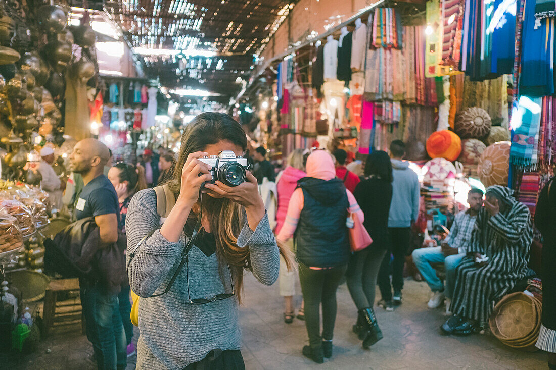 Female tourist taking photo in Jemaa el-Fnaa souk, Marrakesh, Morocco