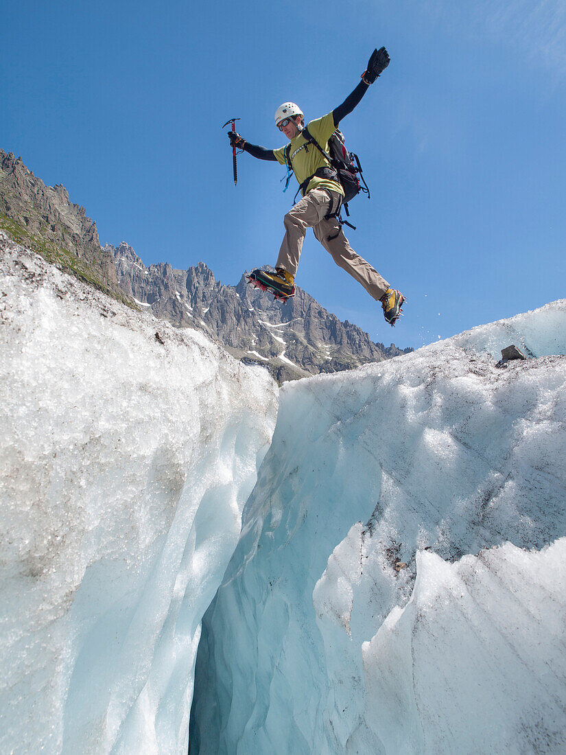 A mountain climber is jumping over a crevasse on Mer de Glace, a famous glacier in the Mont Blanc range.