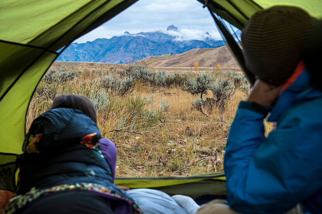 Camping couple looking at view of mountains outside tent, Jackson, Wyoming, USA
