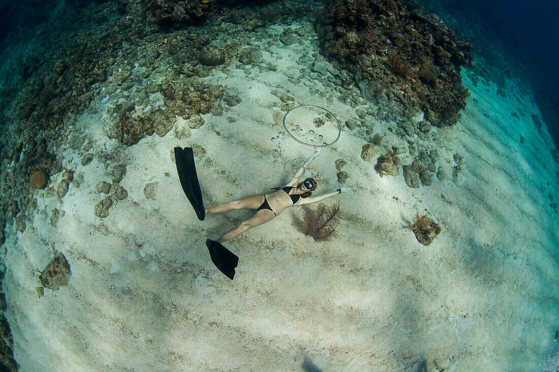 Woman blowing ring bubbles, freediving underwater off coast of Roatan Islands reef, Honduras