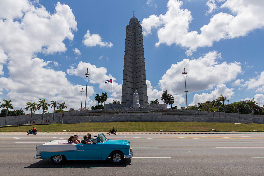 Tourists driving vintage car at Plaza de la Revolucion with Jose Marti Memorial in background, Havana, Cuba