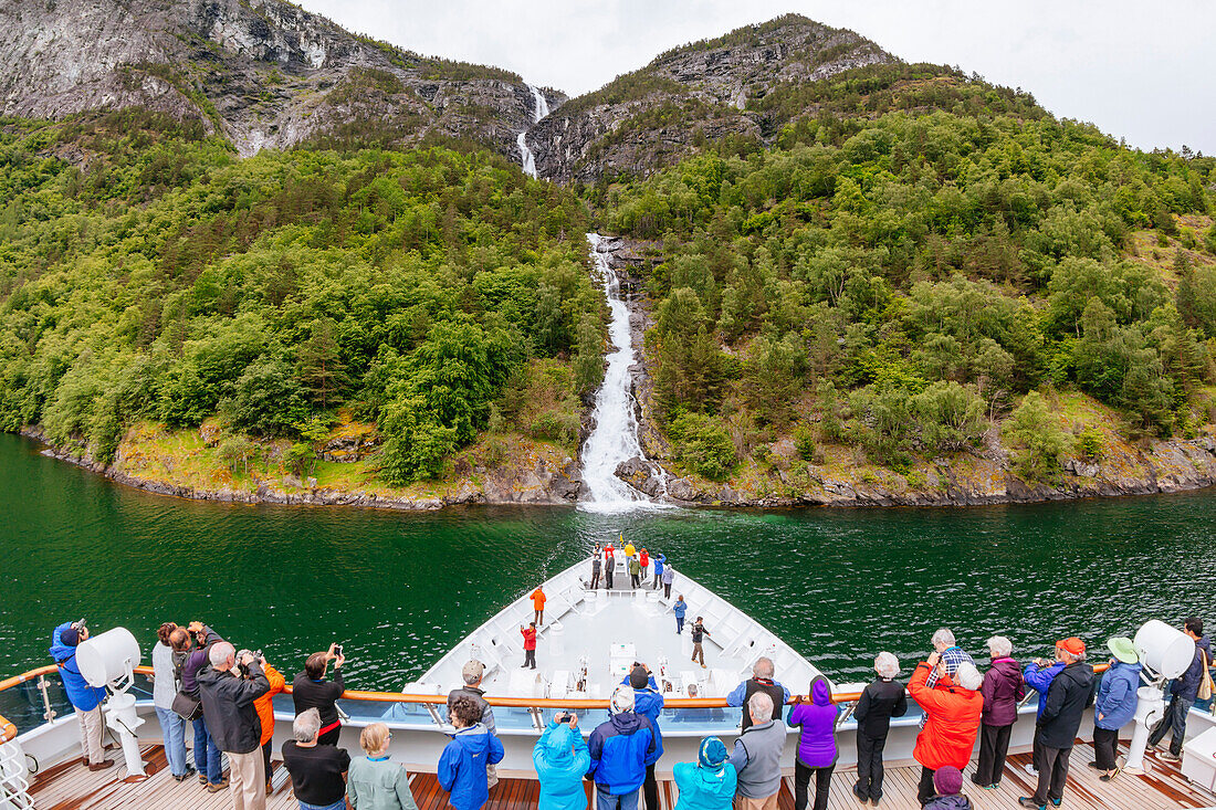 Large group of passengers on ship looking at view and photographing waterfall at Naeroyfjord, Sogn og Fjordane, Norway