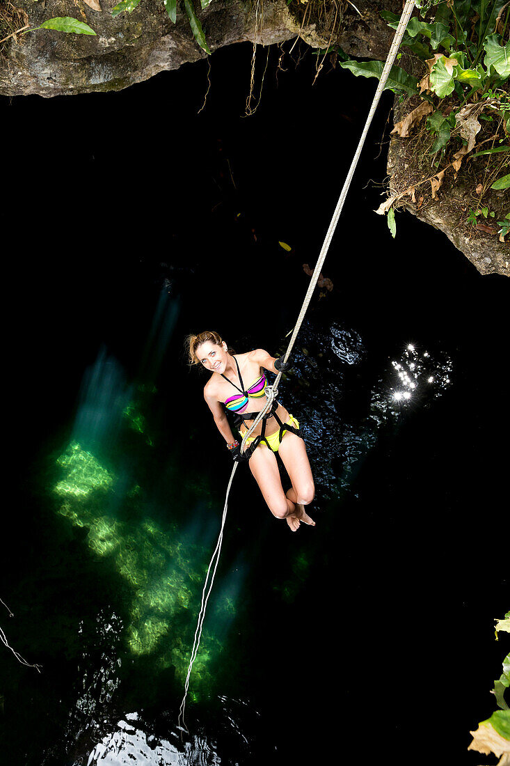 Female tourist rappels down rope into Gran Cenote Maya, near archeological site of Ek Balam in Valladolida, Yucatan, Mexico