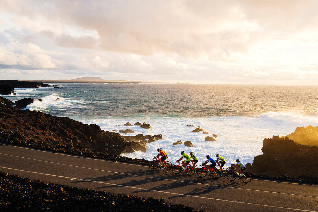 Group of cyclists pedaling on coastal road, Timanfaya National Park, Lanzarote, Canary Islands, Spain