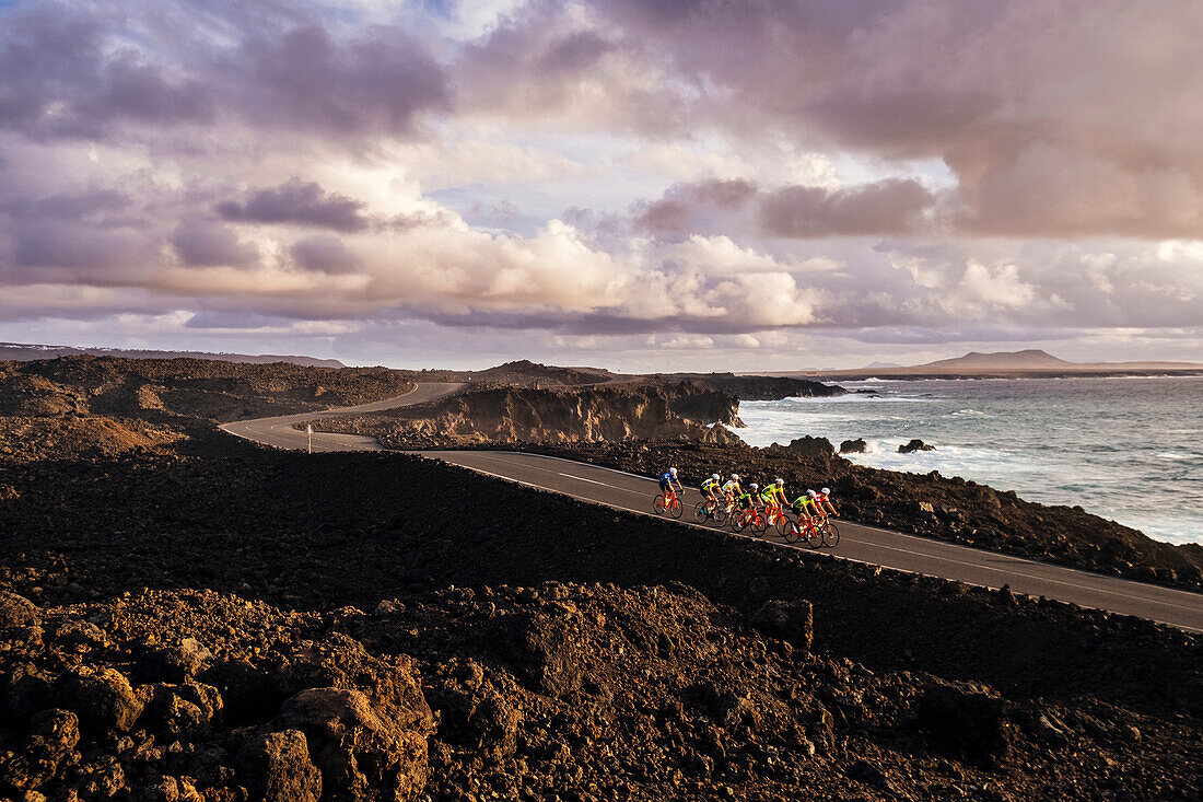 Group of cyclists pedaling on coastal road, Timanfaya National Park, Lanzarote, Canary Islands, Spain
