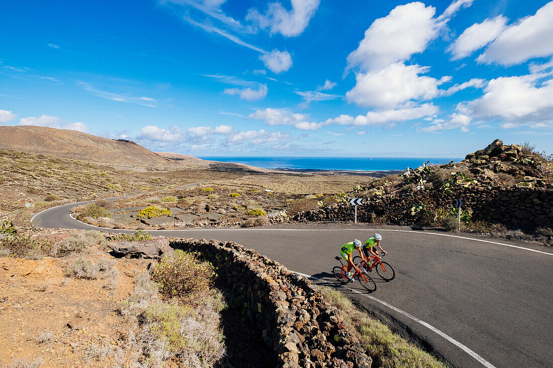 Two road cyclists riding side by side on road, Lanzarote, Canary Islands, Spain