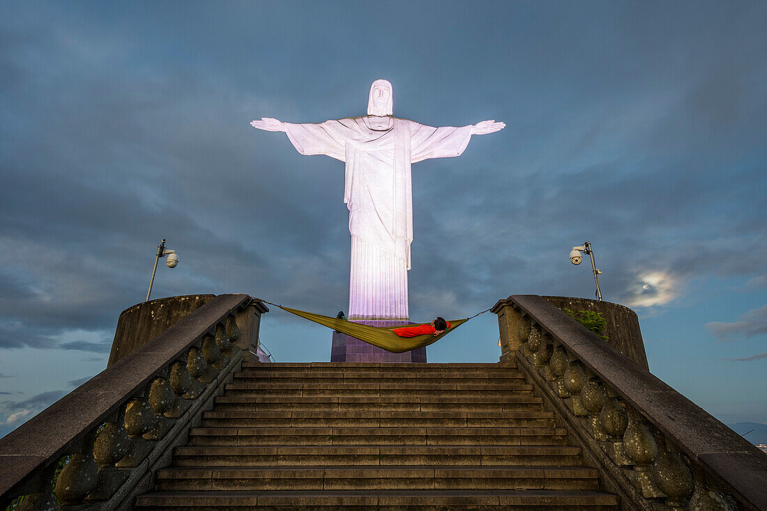 Man lying on hammock during sunrise under Cristo Redentor (Christ the Redeemer) on top of Morro do Corcovado (Corcovado Mountain), Rio de Janeiro, Brazil