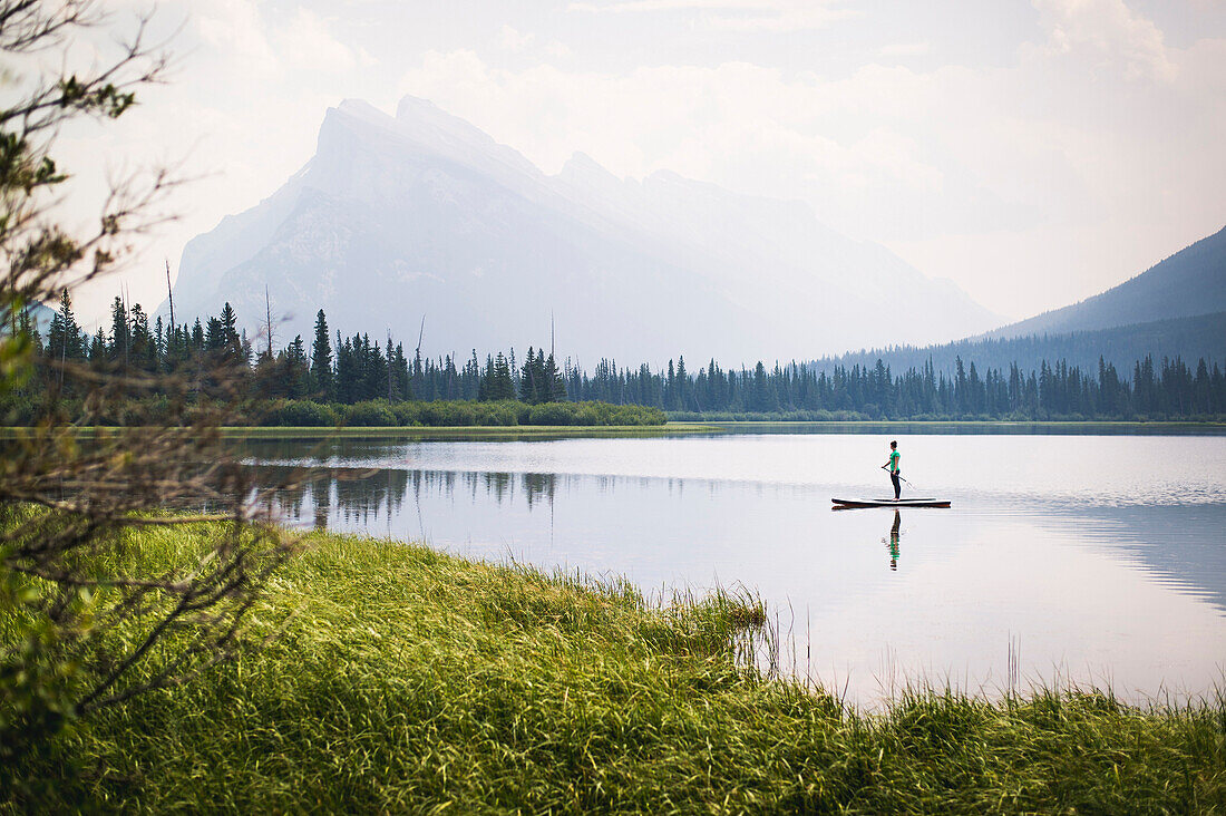 Woman paddleboarding across one of Vermillion Lakes with Mount Rundle in background, Alberta, Canada