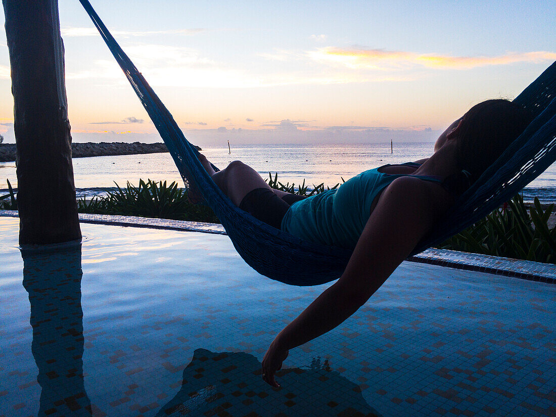 Woman laying in hammock at sunrise and looking out at ocean, Puerto Morelos, Yucatan Peninsula, Mexico
