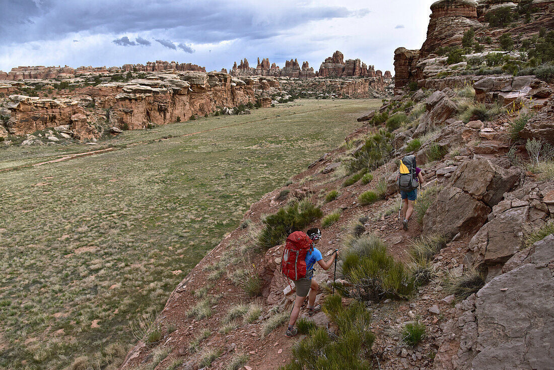 Two female backpackers on trail overlooking The Needles in Canyonlands National Park, Moab, Utah, USA