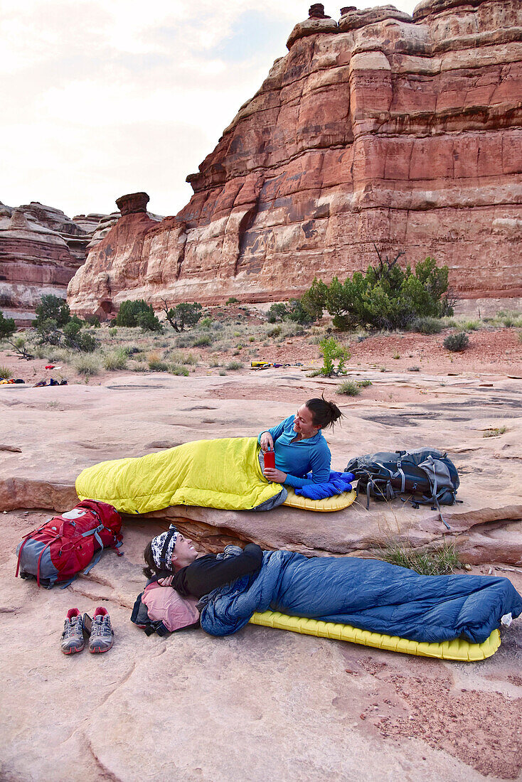 Side view of two women in sleeping bags while camping in Canyonlands National Park, Moab, Utah, USA