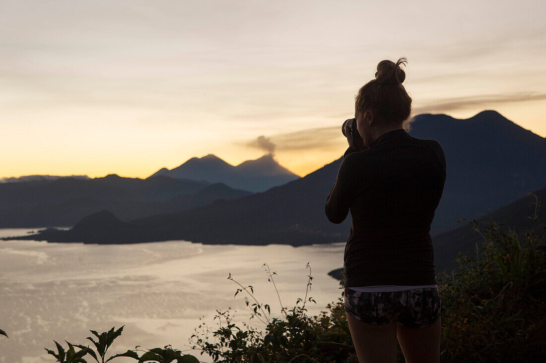 Rear view of woman taking pictures at sunrise of Lake Atitlan, Guatemala