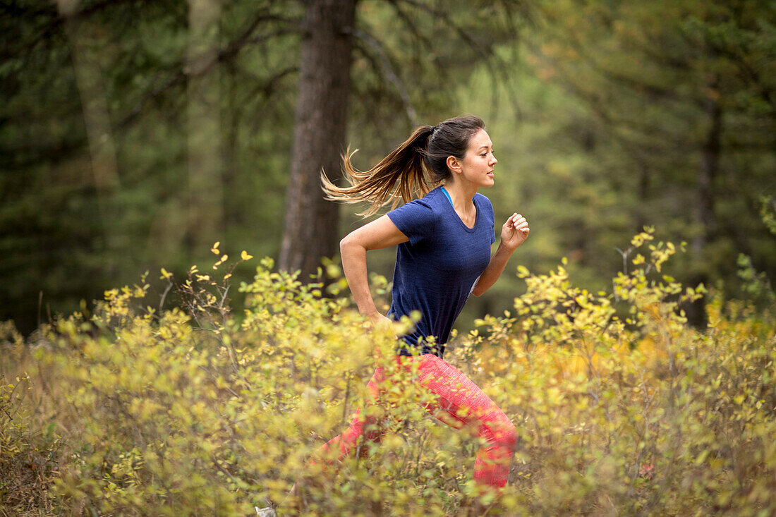 Side view of young athletic woman trail running in forest