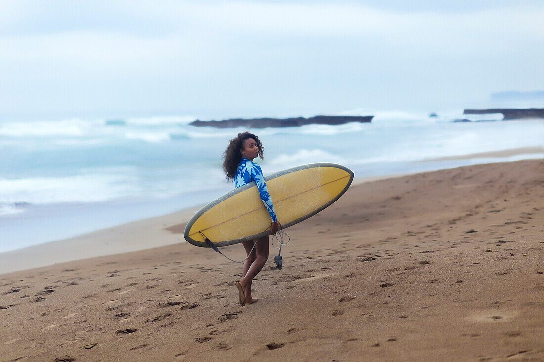 Vacation photo of lone woman carrying surfboard at beach