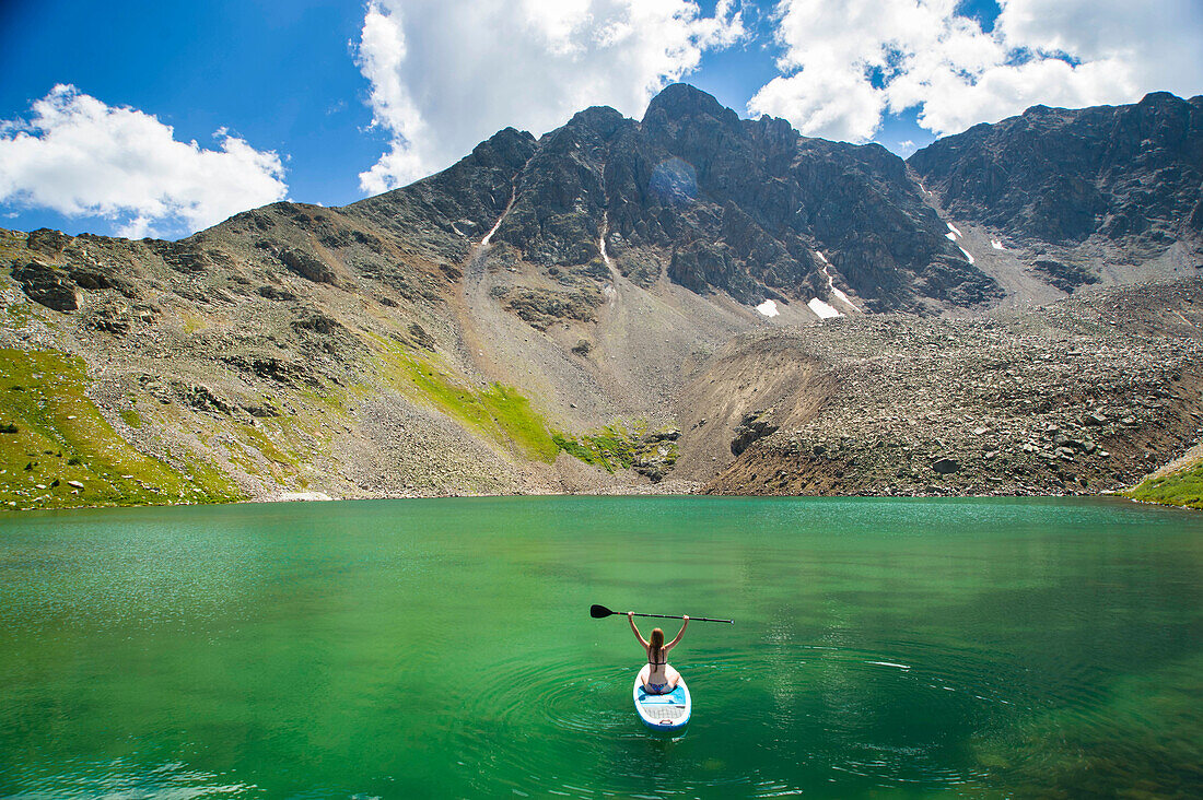 Aerial view of young female sitting on paddle board on high alpine lake in Aspen, Colorado, USA