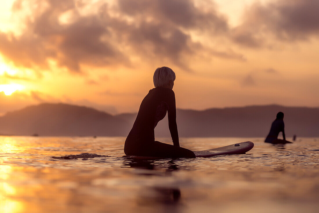 Side view of female surfer in wetsuit in sea at sunset
