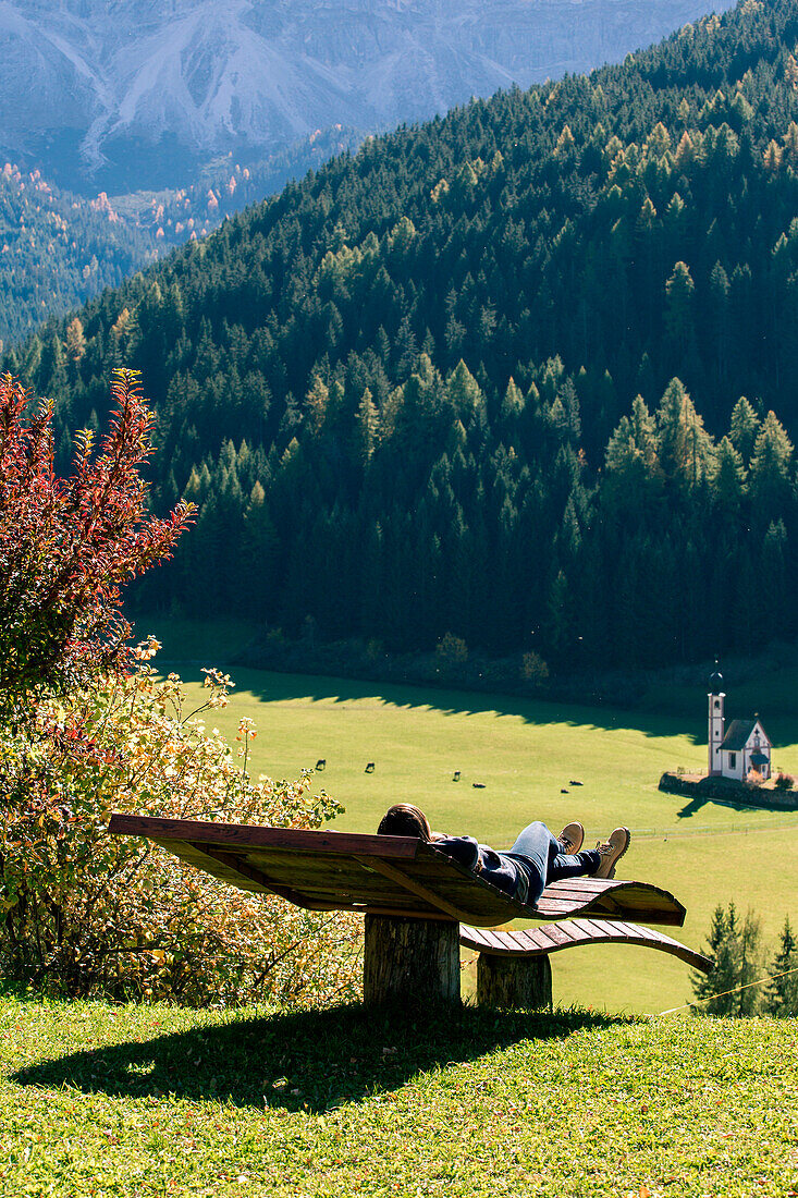 Girl relaxing on a bench in the Italian Dolomites Alps, Funes Valley, Trentino Alto Adige, Italy
