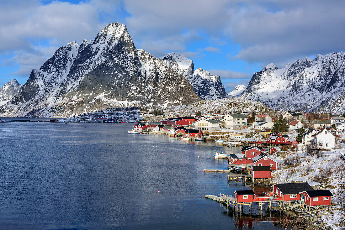 Verschneite Berge mit Fischerhäuser und Hafen von Reine, Reine, Lofoten, Nordland, Norwegen