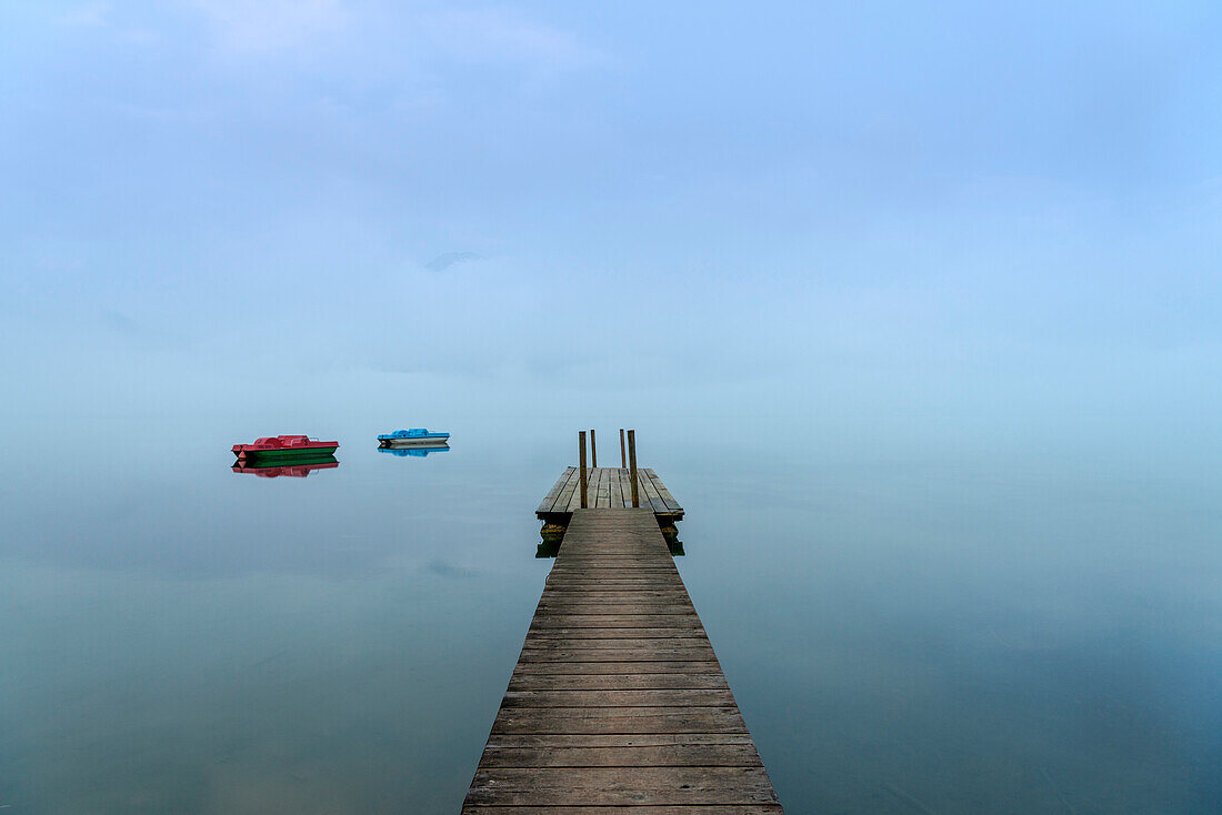 Kochel am See, Bad Tölz-Wolfratshausen district, Upper Bavaria, Germany, Europe. Jetty with two pedal boats in the Kochel Lake at dawn