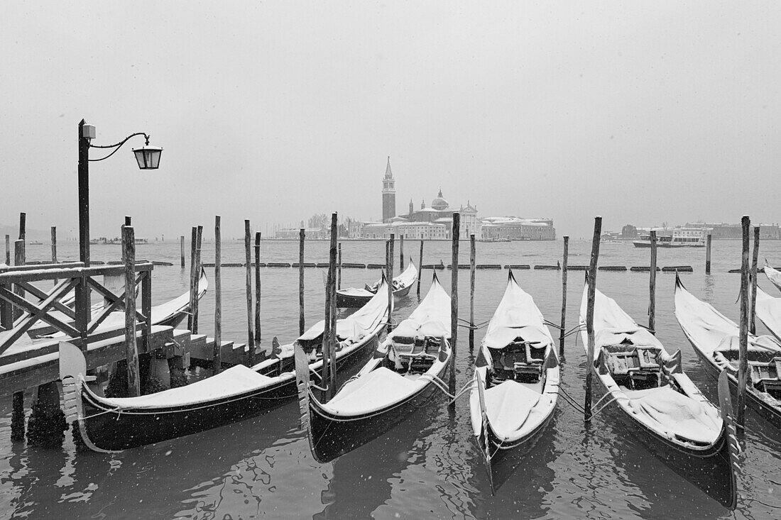 Some traditional venetian gondolas moored at Riva degli Schiavoni during a snowfall, Venice, Veneto, Italy