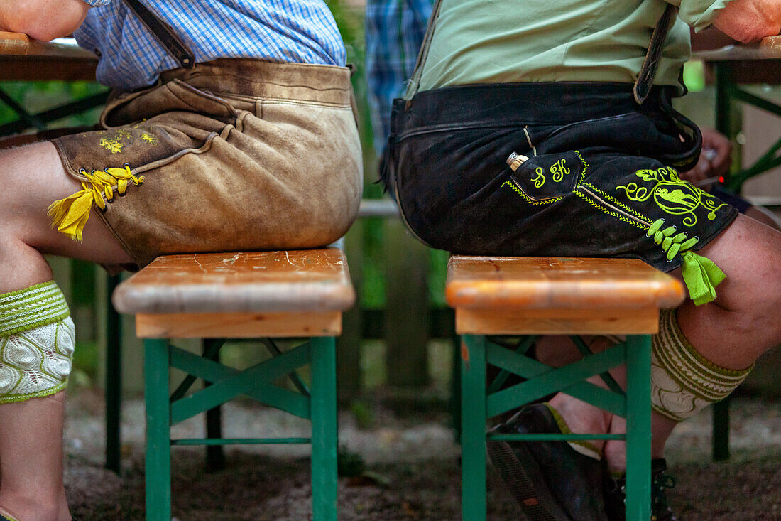 Zwei Männer in kurzen Lederhosen sitzen Rücken an Rücken auf Bänken im Biergarten; Detailansicht