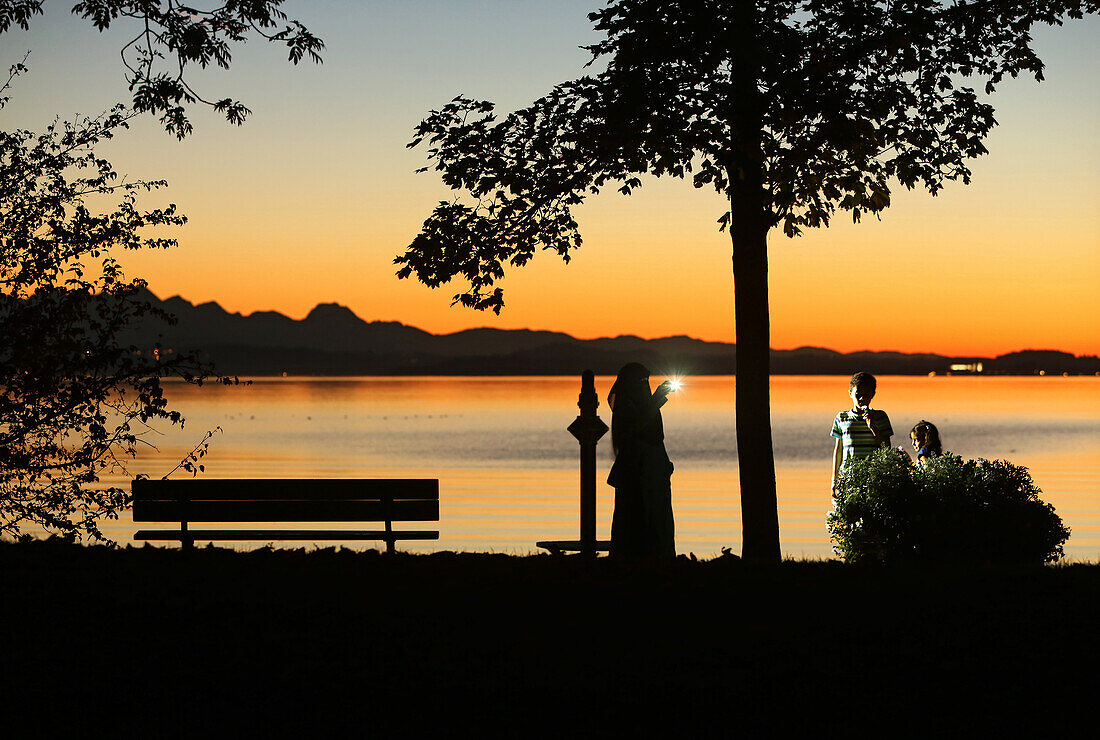 In the last evening light veiled woman makes a cell phone photo of your children on the banks of Lake Chiemsee