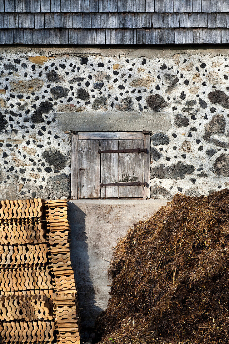 Stacked roof tiles and dung heap under a small wooden door; slag stone wall and wood shingle weather coat