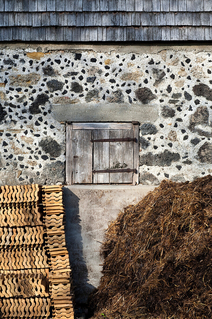 aufgestapelte Dachziegel und Misthaufen unter kleinem Holz-Türchen; Schlackestein-Mauer und Holzschindel-Wettermantel