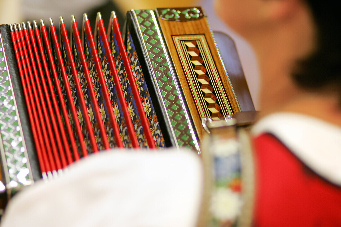 Frau im bayerischen Dirndl spielt die diatonische Ziach; Blick über die Schulter auf den verzierten Balg der Harmonika