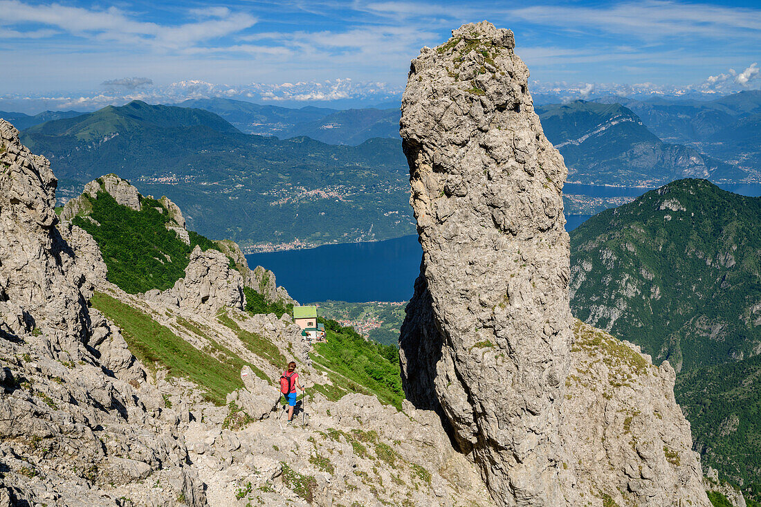 Woman hiking near rock spire towards hut rifugio Rosalba, lake lago di Como in background, from Grignetta, Grigna, Bergamasque Alps, Lombardy, Italy