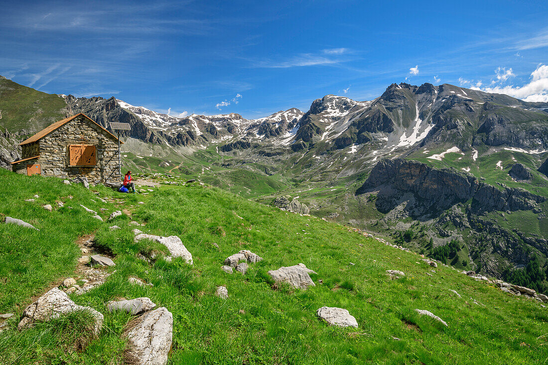 Woman hiking sitting at hut rifugio Stroppia, hut rifugio Stroppia, Val Maira, Cottian Alps, Piedmont, Italy