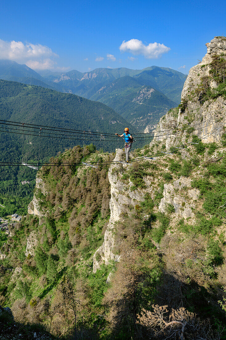 Woman climbing fixed rope route crossing ropeway, Ferrata di Camoglieres, Val Maira, Cottian Alps, Piedmont, Italy