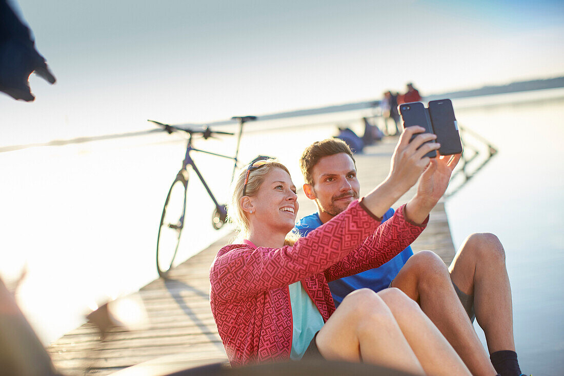 junge Frau  und junger Mann mit Fahrrädern auf Steg am Seeufer machen en Selfie, Starnberger See, Bayern, Deutschland