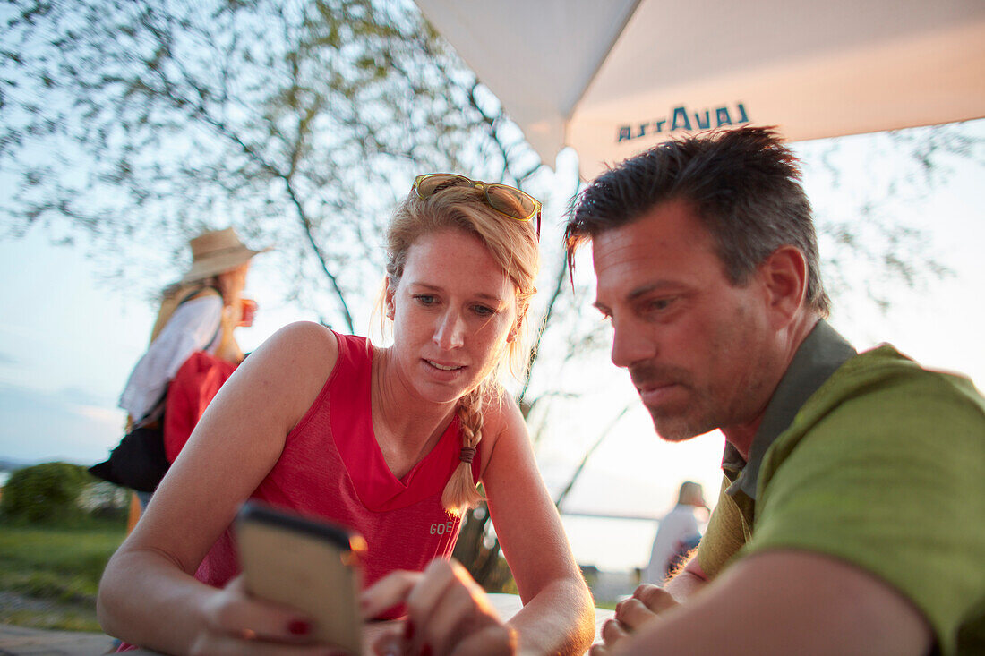 Young  couple using mobile phone on  a break on bicycle tour, Ambach, bavaria, germany