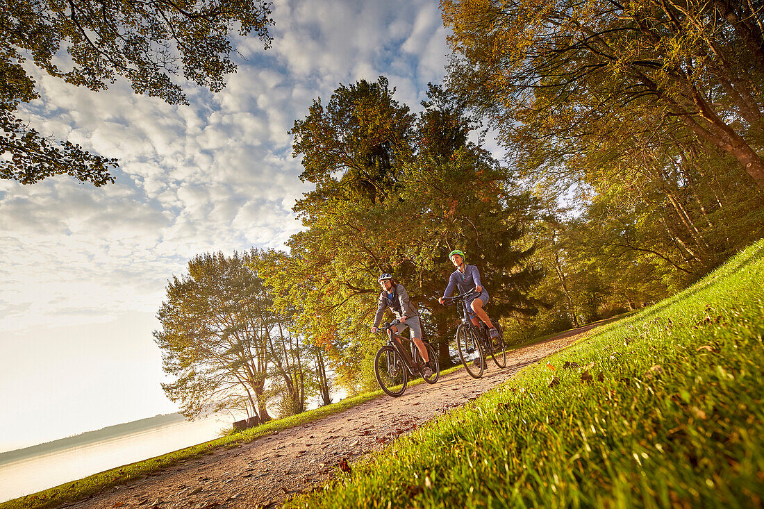 Young  woman on touring bike, young man on touring eBike on tour at lakeside, lake Starnberg, bavaria, germany