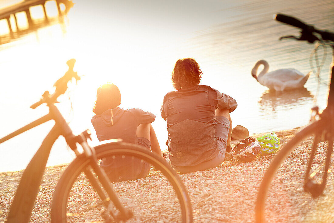 junge Frau  und junger Mann Paar sitzen mit Fahrrädern am Seeufer, Starnberger See, Bayern, Deutschland