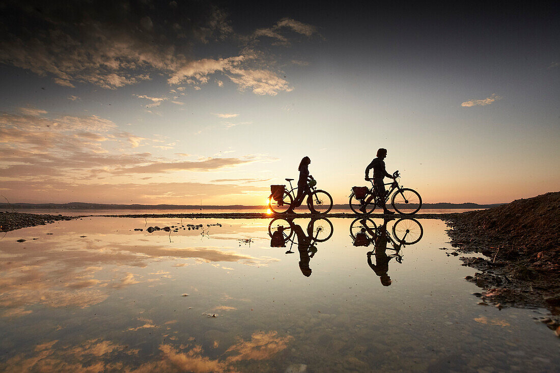 Young  woman on touring bike, young man on touring eBike on tour, lakeshore, Muensing, lake starnberg, bavaria, germany