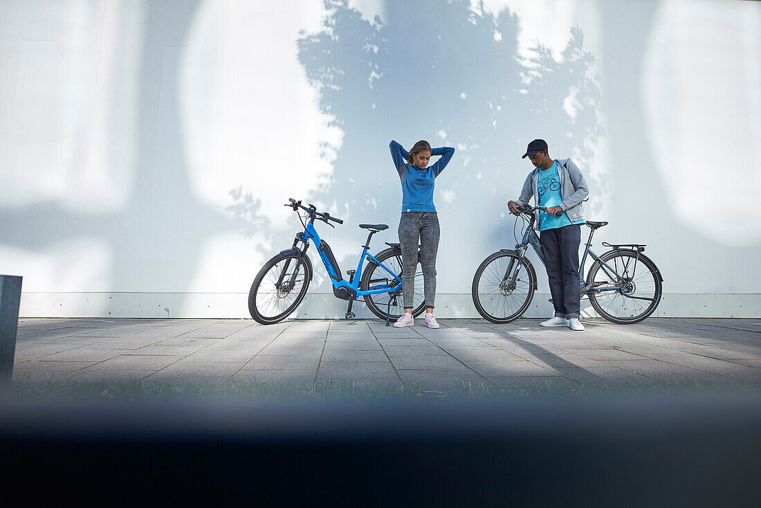 Young  woman young man with eBikes downtown, Munich, bavaria, germany