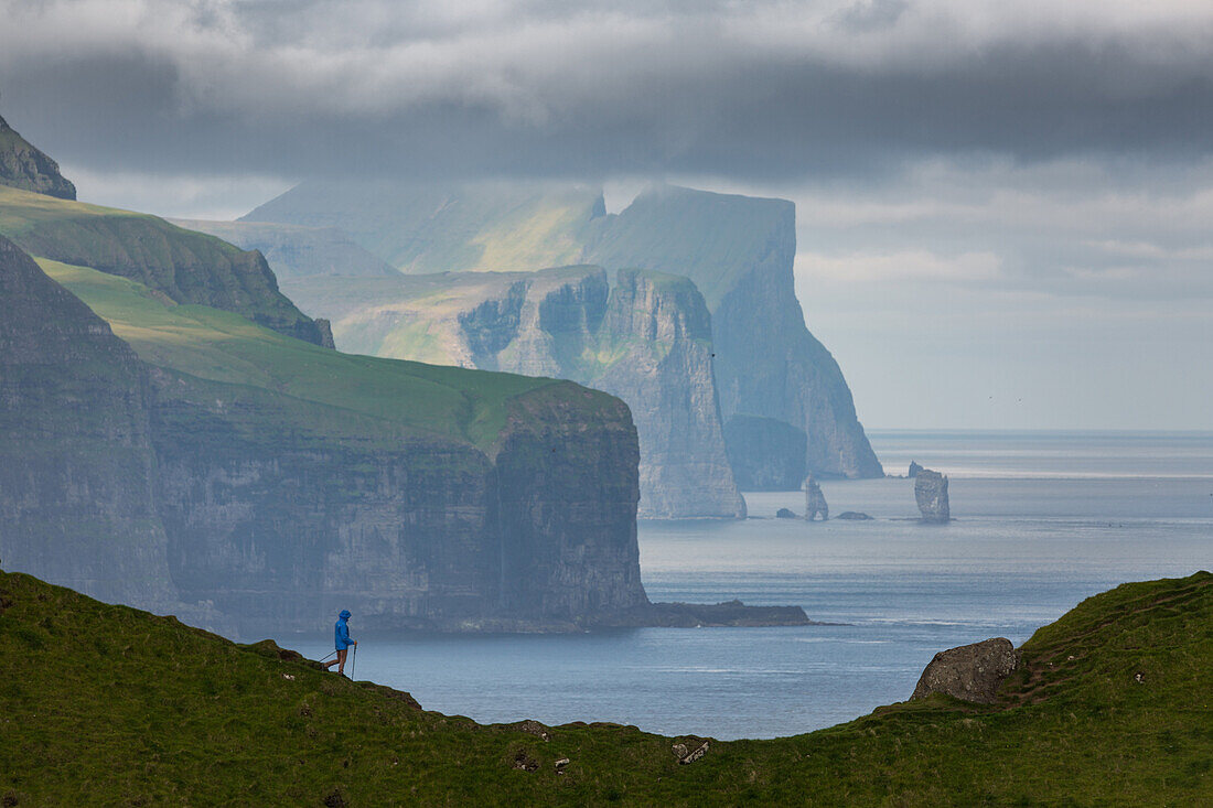 hiker following a steep coastal trail, tall cliffs over the sea in the background, kalsoy, faroe islands, denmark