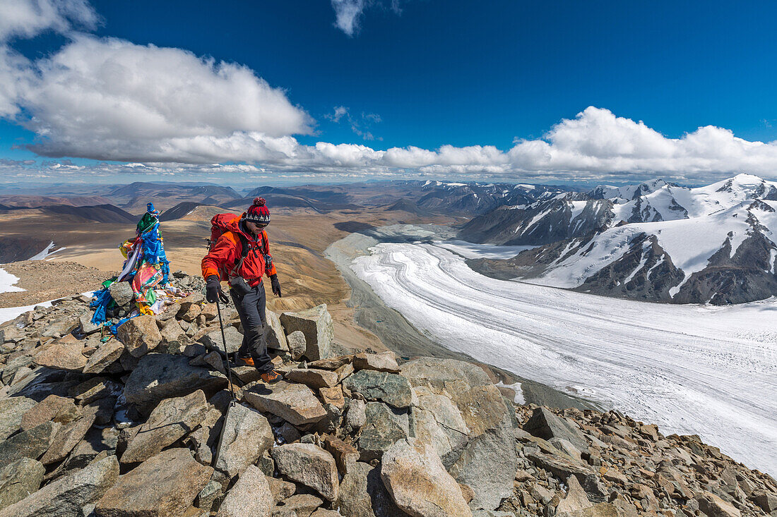hiker at the summit of mount malchin, tavan bogd massif in the background, altai, bayan-olgii province, mongolia