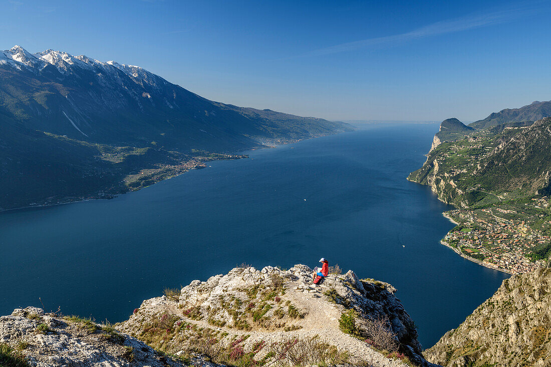 Frau beim Wandern sitzt auf Felssporn und blickt auf Gardasee und Gardaseeberge, Gardasee, Gardaseeberge, Trentino, Italien