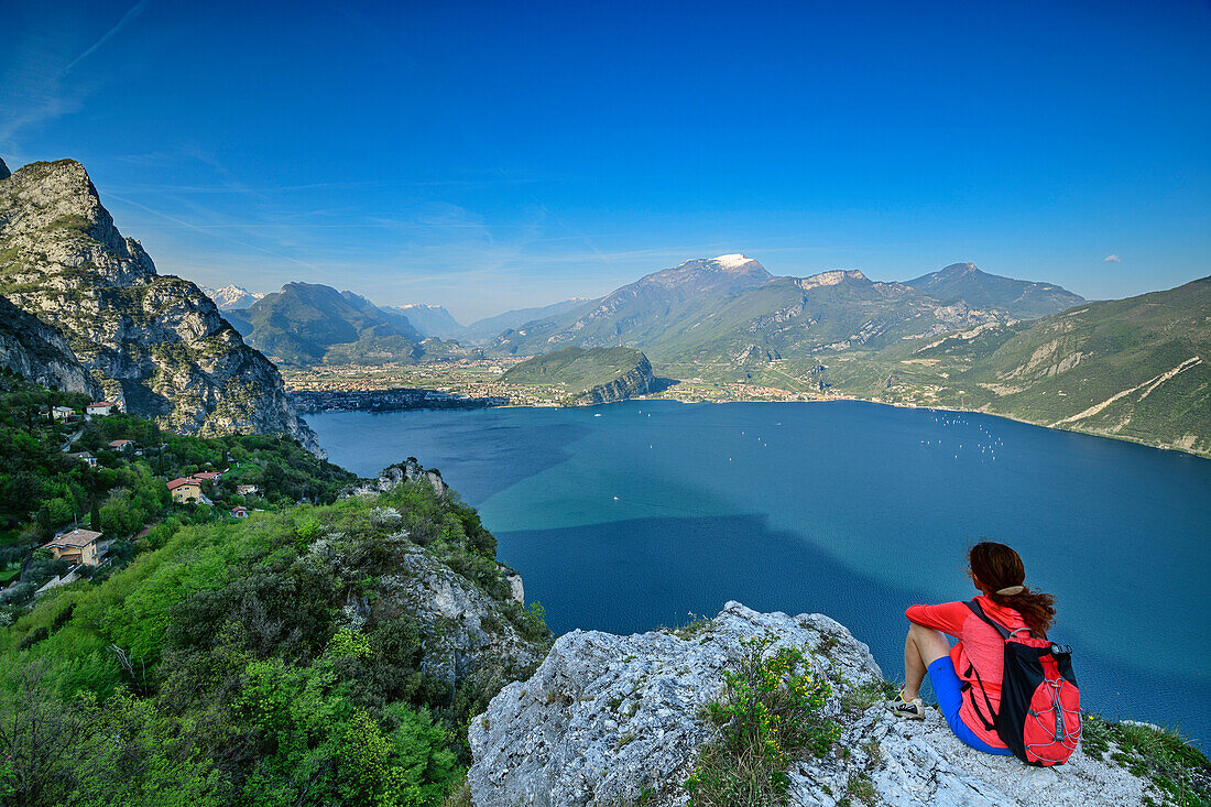 Frau beim Wandern sitzt auf Felssporn und blickt auf Gardasee und Gardaseeberge, Gardasee, Gardaseeberge, Trentino, Italien