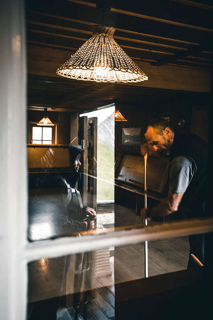 Bergsteigerin spiegelt sich im Fenster während Almwirt kehrt,E5, Alpenüberquerung, 3. Etappe, Seescharte, Inntal, Tirol, Österreich, Memminger Hütte zur Unterloch Alm