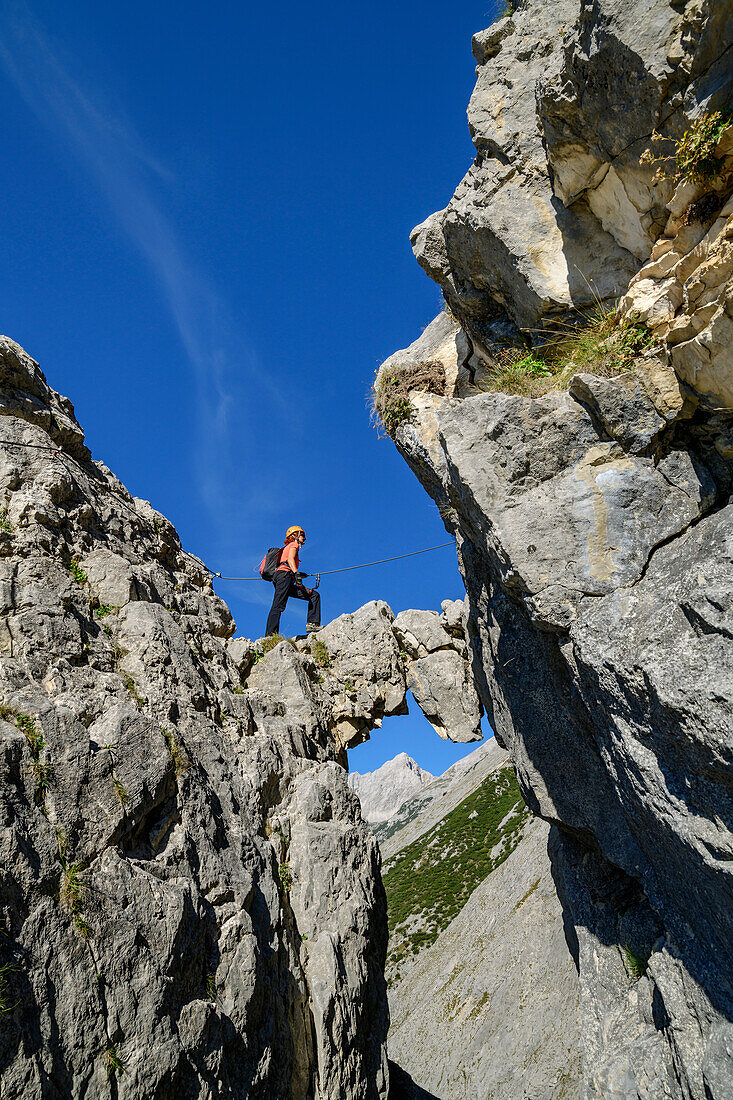 Frau steigt über Felsbogen am Klettersteig zum Bettelwurf auf, Absamer Klettersteig, Bettelwurf, Karwendel, Tirol, Österreich