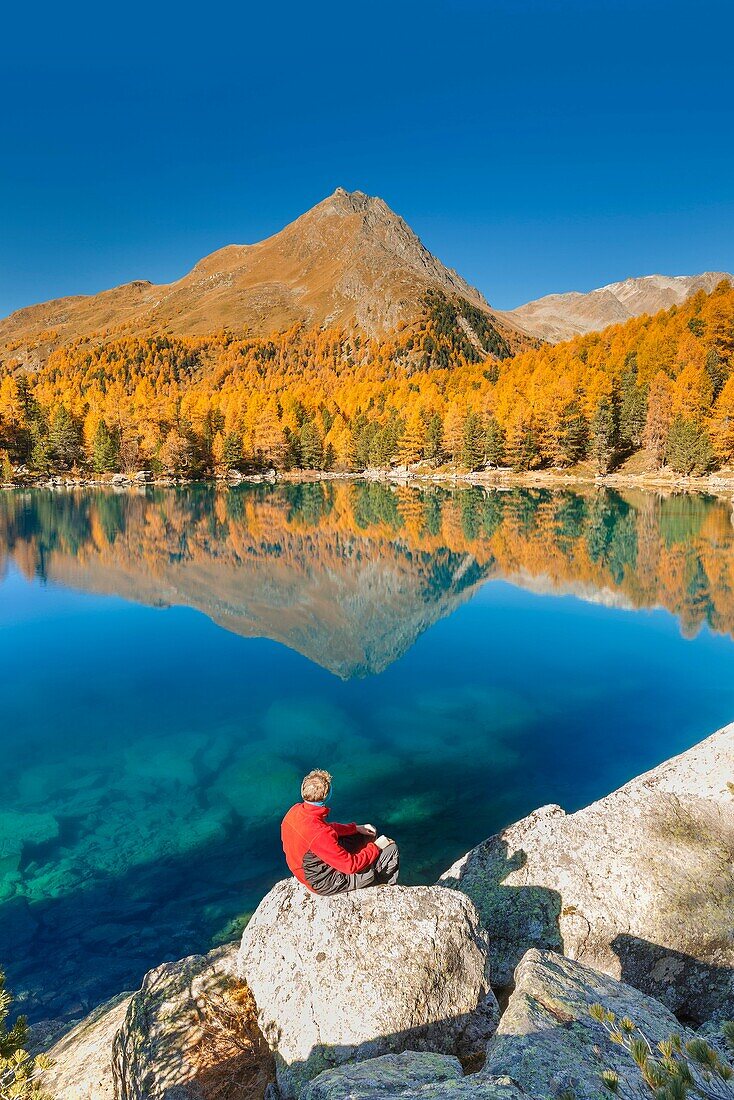 Hiker take a break to admire lake Saoseo in a perfect autumn day, Poschiavo, val di Campo, Canton of Graubunden, Switzerland, Europe.