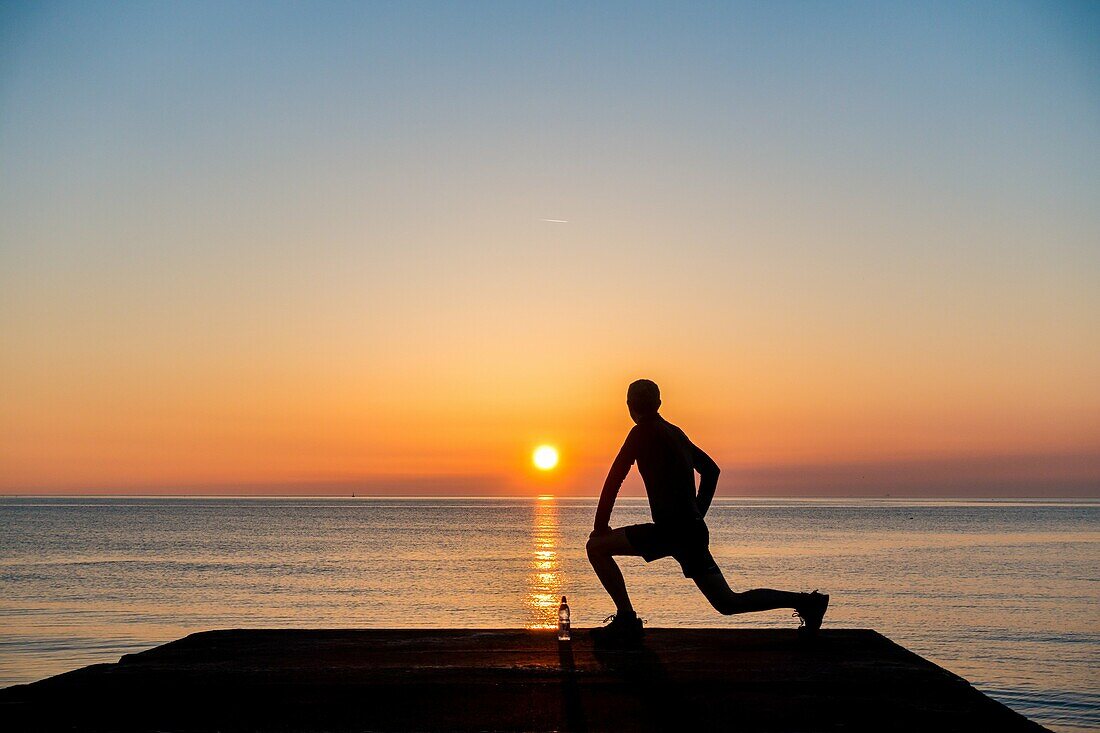 Seaton Carew, County Durham, north east England. United Kingdom. A jogger looks out over the North sea at sunrise.