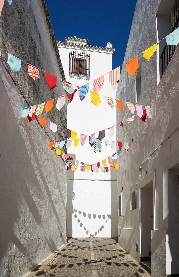 Alley and brilliantly whitewashed houses in the hilltop White Town of Arcos de la Frontera. The little colourful flags are remains of a feast that took place the previous week. Cadiz province, Andalusia, Spain.