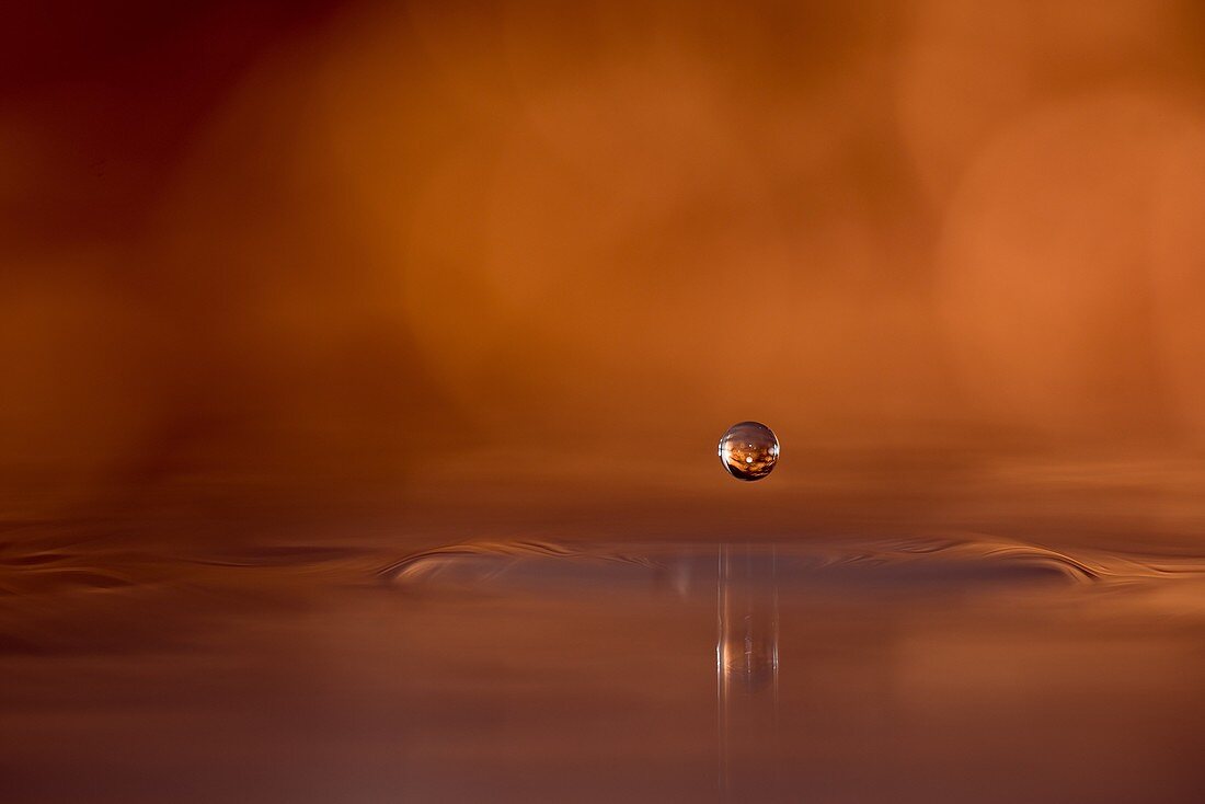 Copper colored water drop suspended above the surface of the water